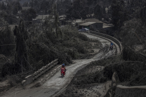 14 January 2020 – Motorcyclists cross a bridge partially blocked by ash-laden trees after the Taal Volcano eruption, in the municipality of Laurel, in Batangas, Philippines.