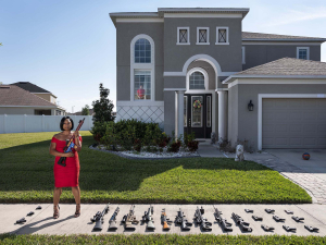 12 April 2019 – Avery Skipalis (33) stands with her firearms in front of her house in Tampa, Florida, USA. Her son looks on from a window. Avery joined the US Air Force when she was 17, and after serving in the UAE, Japan and Germany, left to start a company that offers firearms safety classes to adults and children.