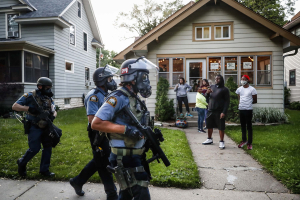 28 May 2020 – Protesters and residents watch as police in riot gear walk down a residential street, in St Paul, Minnesota, USA.