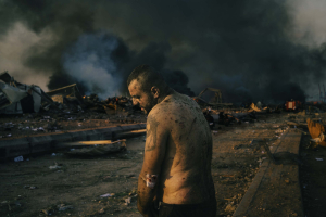 4 August 2020 – An injured man stands near the site of a massive explosion in the port area of Beirut, Lebanon, while firefighters work to put out the fires that engulfed warehouses after the blast.