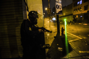 12 November 2020 – A police officer armed with what appears to be a pellet shotgun stands off against protesters, who try to dazzle him with laser beams, in Lima, Peru.