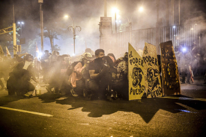 14 November 2020 – Demonstrators shelter from tear gas and rubber bullets, behind shields reading ‘Power to the people’, in Lima, Peru.